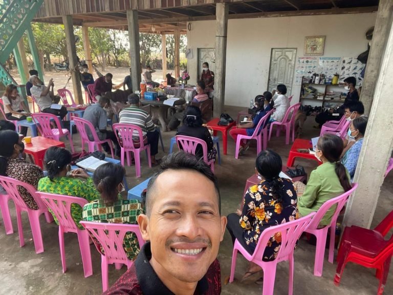 This is a picture of a Cambodian man smiling as he stands in front of a group of children sitting in chairs, taken during the Hope City Stockton Supernatural Lifestyle Training missions trip.